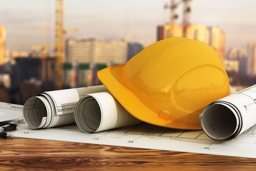 A photo of a hard hat sitting on top of blueprints in front of a construction site.